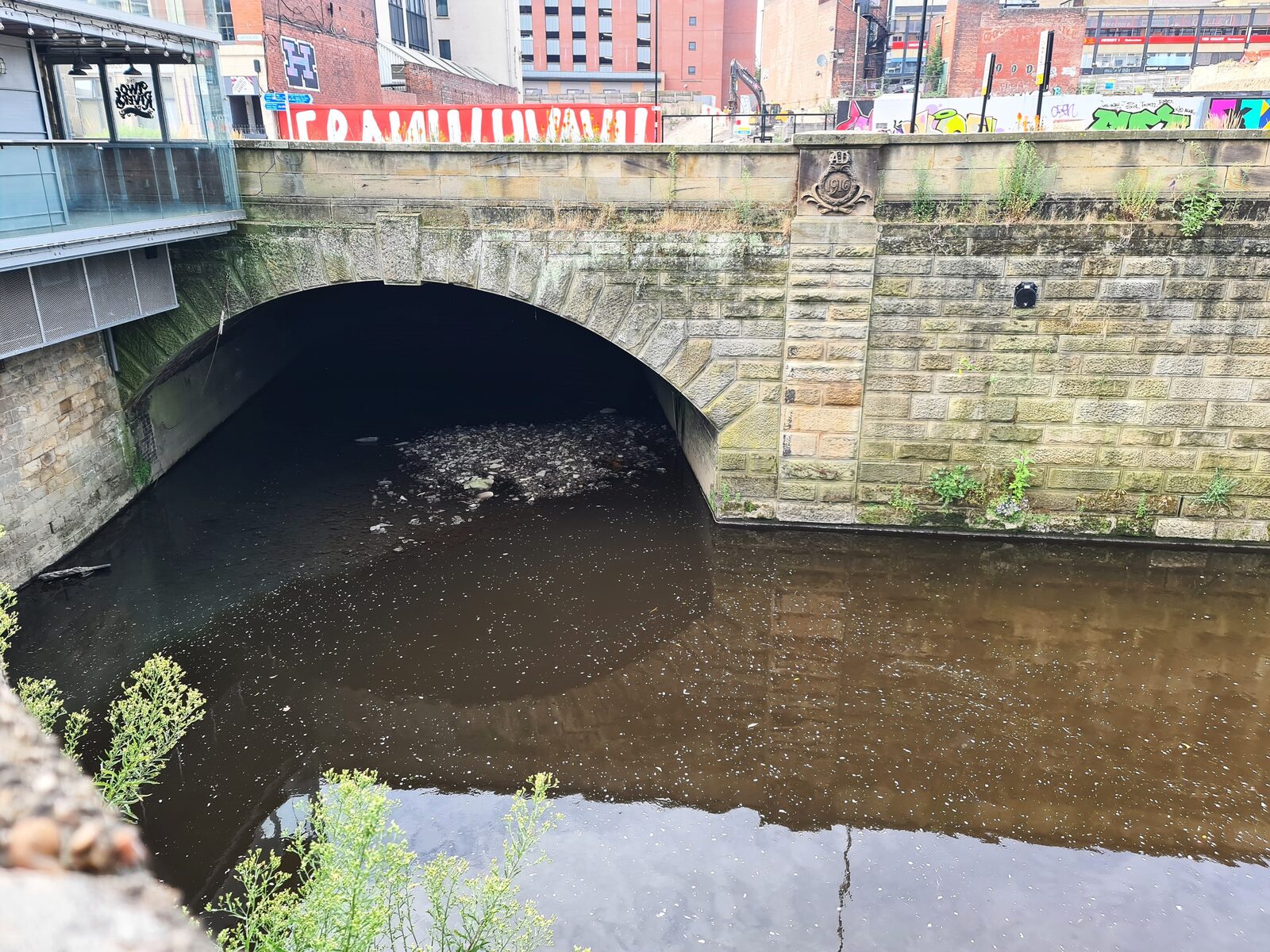 The River Sheaf flowing out of a stone arched culvert into the River Don at Castlegate, Sheffield