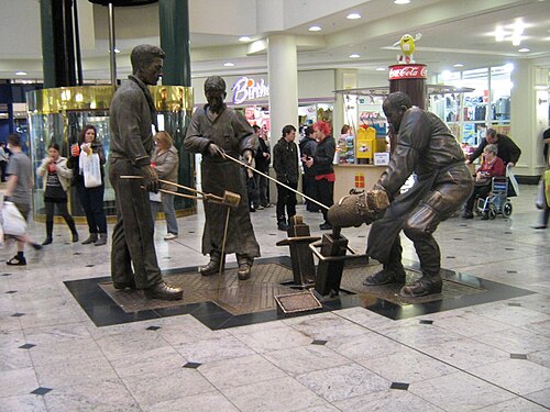 Robin Bell's bronze sculpture Teeming, of steelworkers pouring a crucible, in a shopping centre concourse.