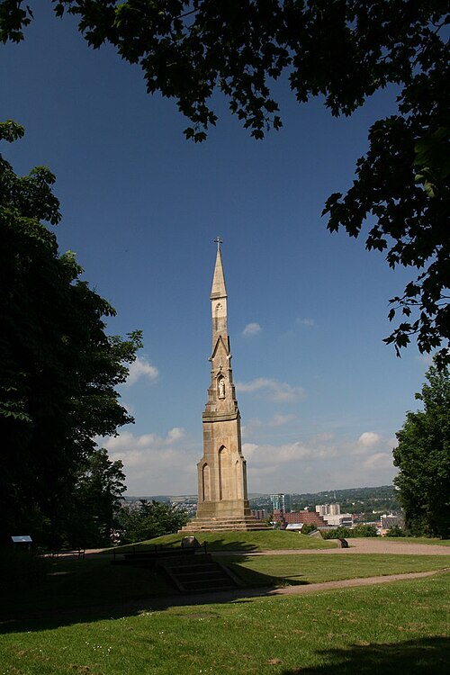 The tall stone spire of the Cholera Monument above Sheffield, seen through trees.