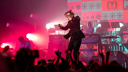 Jarvis Cocker singing with Pulp on a festival stage.
