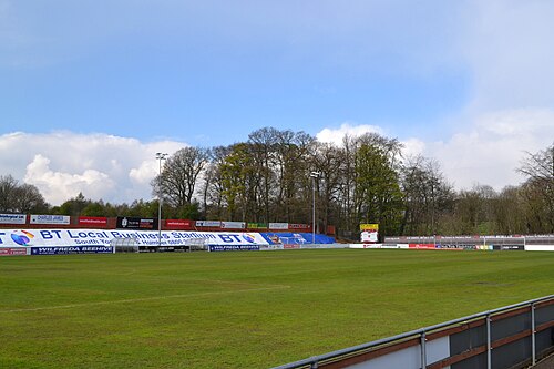A small non-league football ground with a low stand and houses behind.